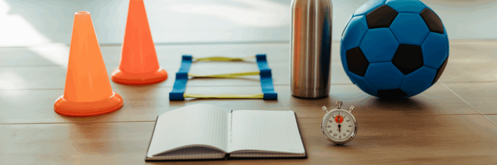Trainingsequipment mit Notizbuch, Stoppuhr und Hütchen als Wochenplan-Symbolik.